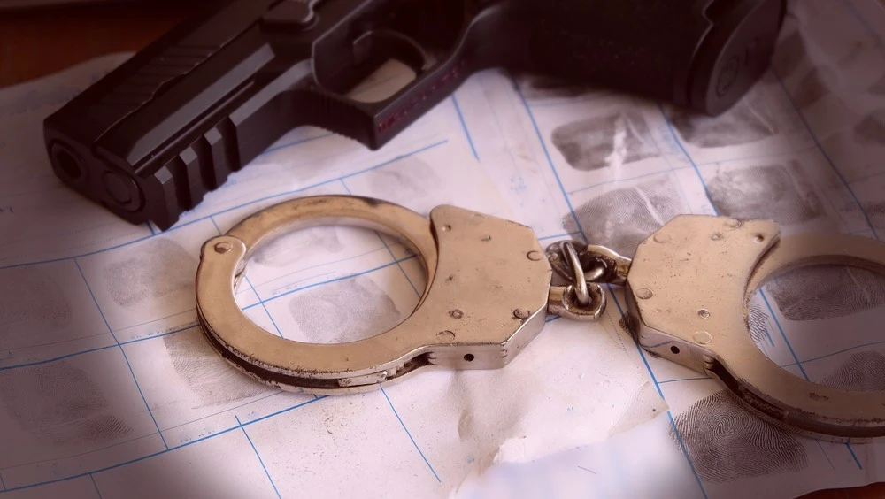 A pair of handcuffs and a gun lie side by side on a dimly lit table, symbolizing the urgent need for skilled legal representation in an aggravated assault case.