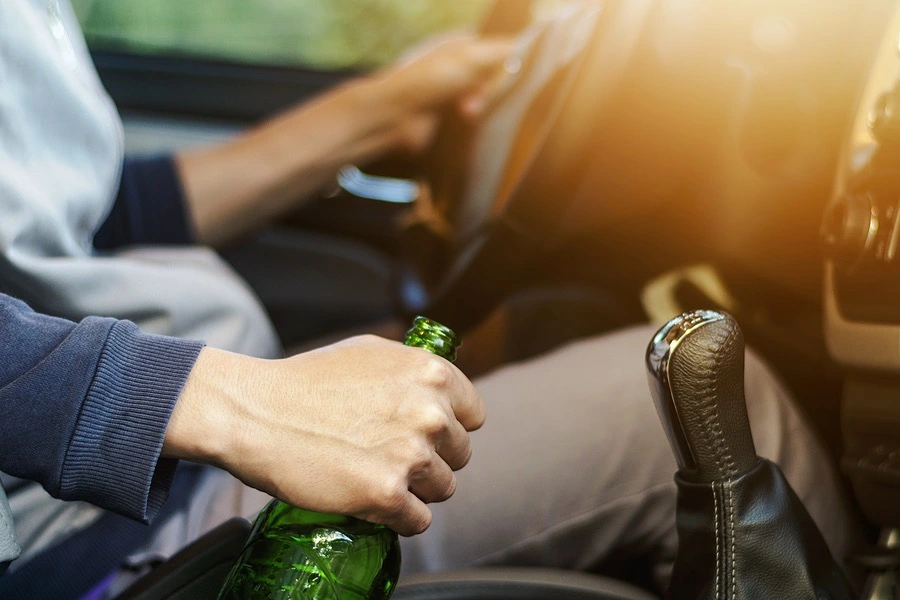 A person with a beer in hand while steering a vehicle, symbolizing a DUI offense