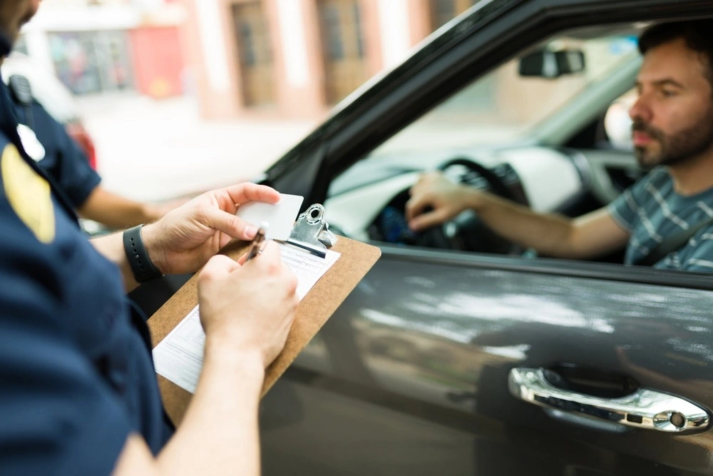 A person receiving a traffic citation from a police officer, looking concerned and thoughtful, as they consider the necessity of discussing attorney fees with a traffic offense lawyer. 